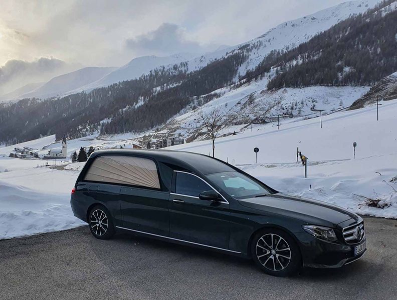 Ein schwarzer Mercedes parkt vor einem schneebedeckten Berg.